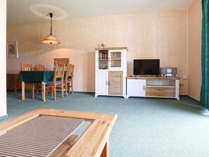 A living room with a dining table, chairs, a TV, speakers, and a cabinet.