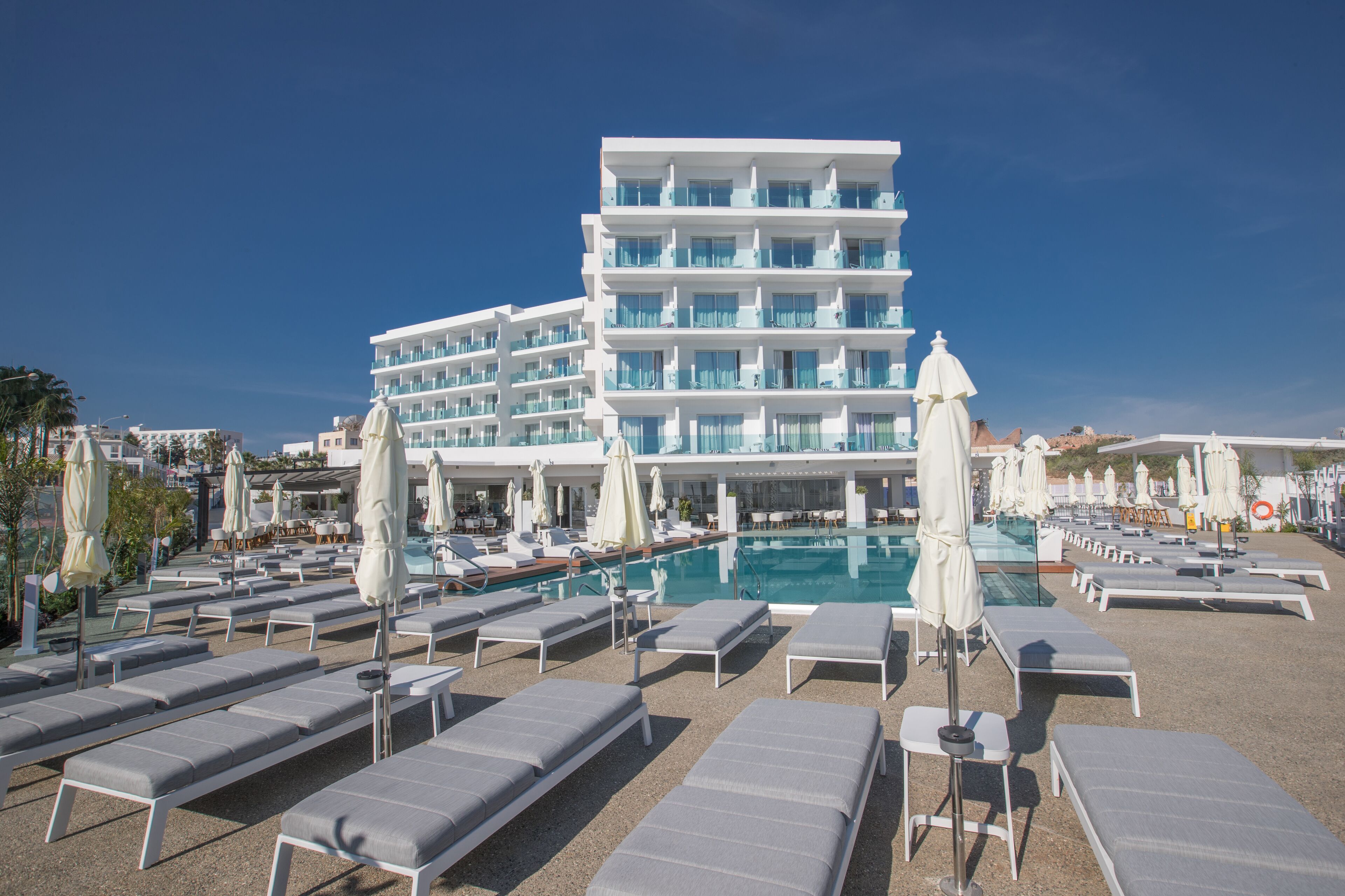 A hotel with multiple floors, a swimming pool, and numerous sun loungers.