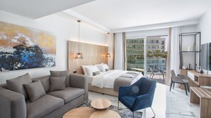 A modern hotel room with a large bed, a sofa, a desk, and a balcony with a city view. - The Blue Ivy Hotel and Suites (Paralimni)