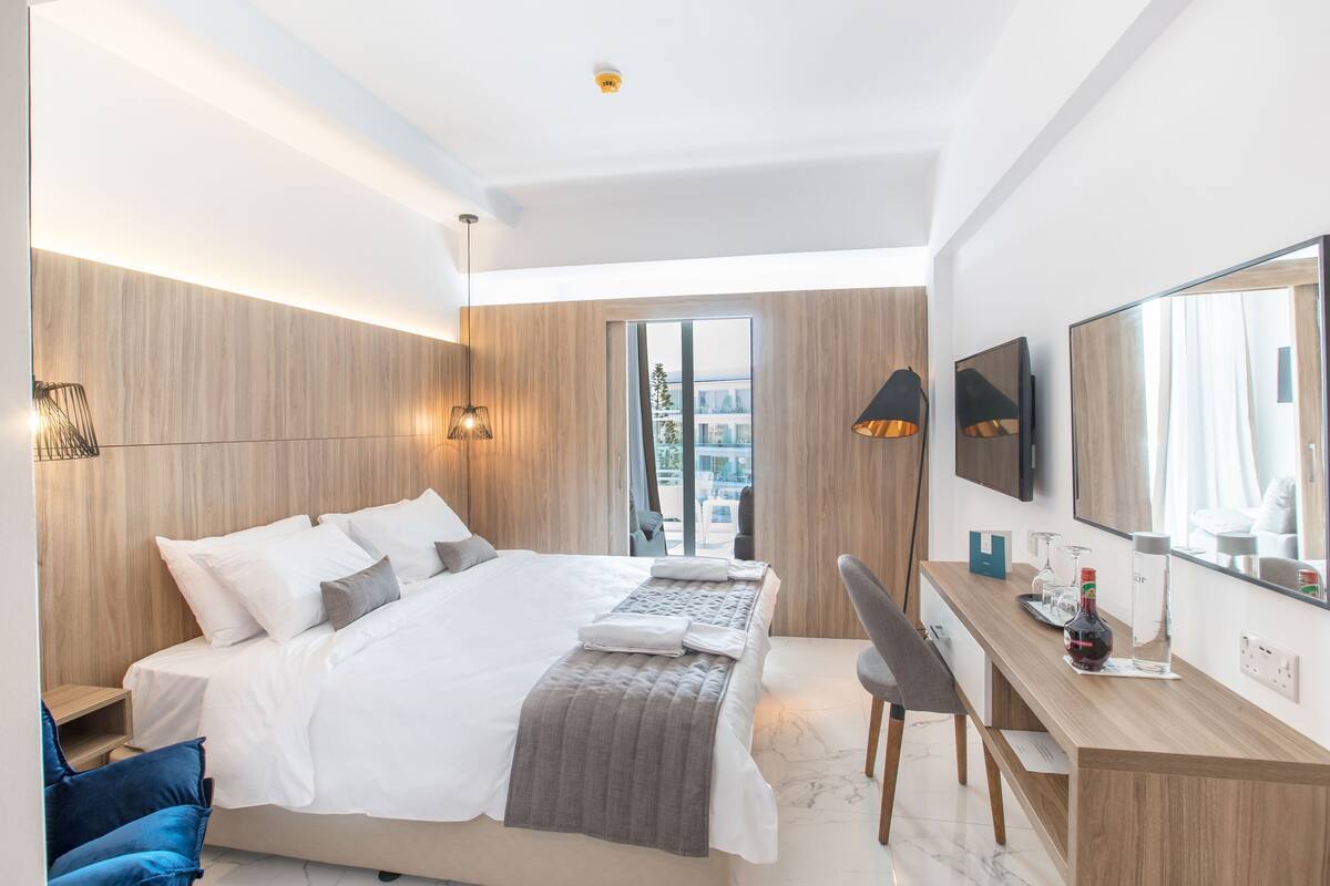 A modern hotel room with a large bed, a desk, and a city view through the window.