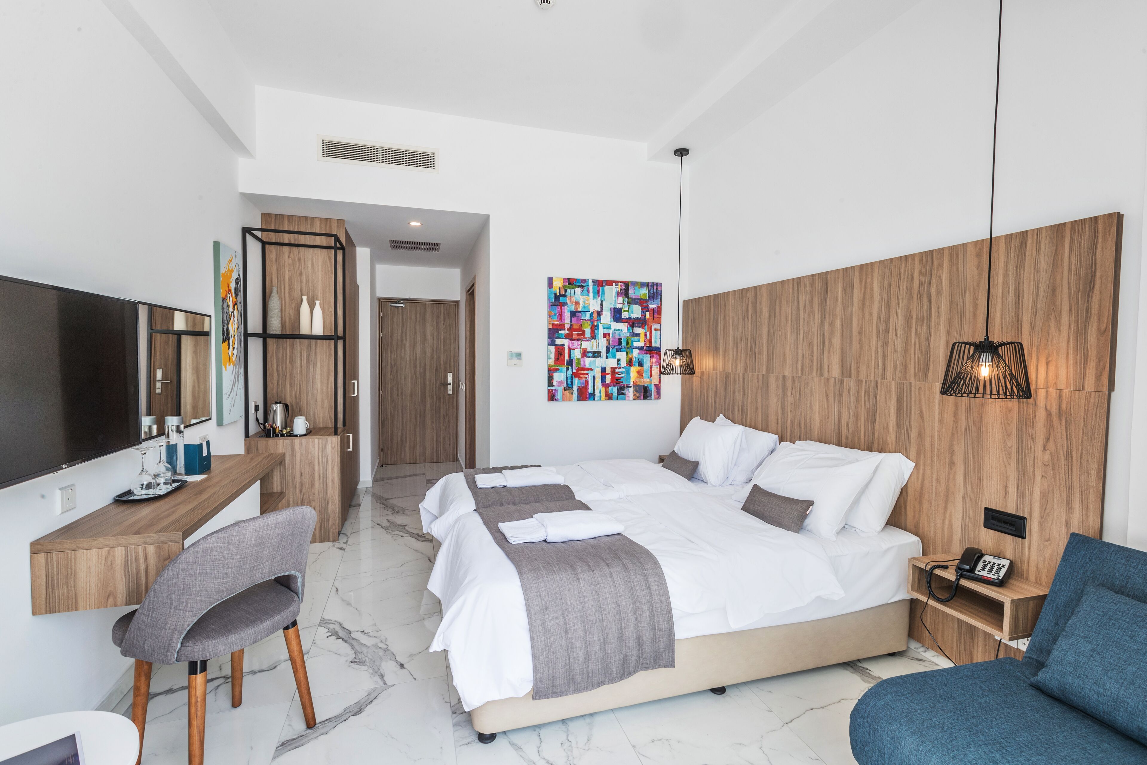 Ein modernes Hotelzimmer mit einem großen Bett, einem Schreibtisch mit Stuhl, einem Fernseher und einem Wandbild.