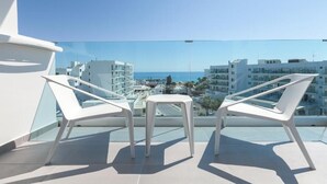 A balcony with two white chairs and a small table, overlooking a cityscape with buildings and a clear sky. - The Blue Ivy Hotel and Suites (Paralimni)