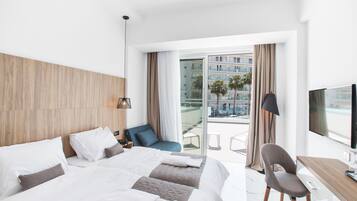 Une chambre d’hôtel moderne dotée d’un grand lit, d’un bureau et d’un balcon offrant une vue sur les palmiers et les immeubles.