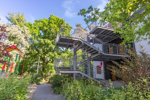 A multi-level outdoor staircase surrounded by greenery, leading to a building with a door and windows.