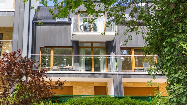 A modern building with a balcony, large windows, and a green fence.