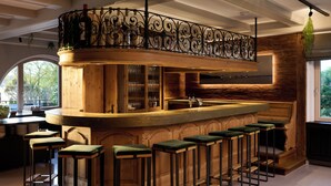 A bar area with a wooden counter, bar stools, and a decorative railing. - Hotel Schloss Berg (Berg)