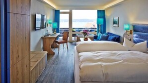 A hotel room with two beds, a desk with a chair, a TV, and a view of the sea. - Hotel Schloss Berg (Berg)