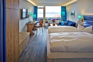 Quarto de hotel com duas camas, uma escrivaninha com cadeira, televisão e vista para o mar.