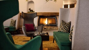 A cozy living room with a fireplace, green and grey upholstered furniture, and a chessboard. - Hotel Schloss Berg (Berg)