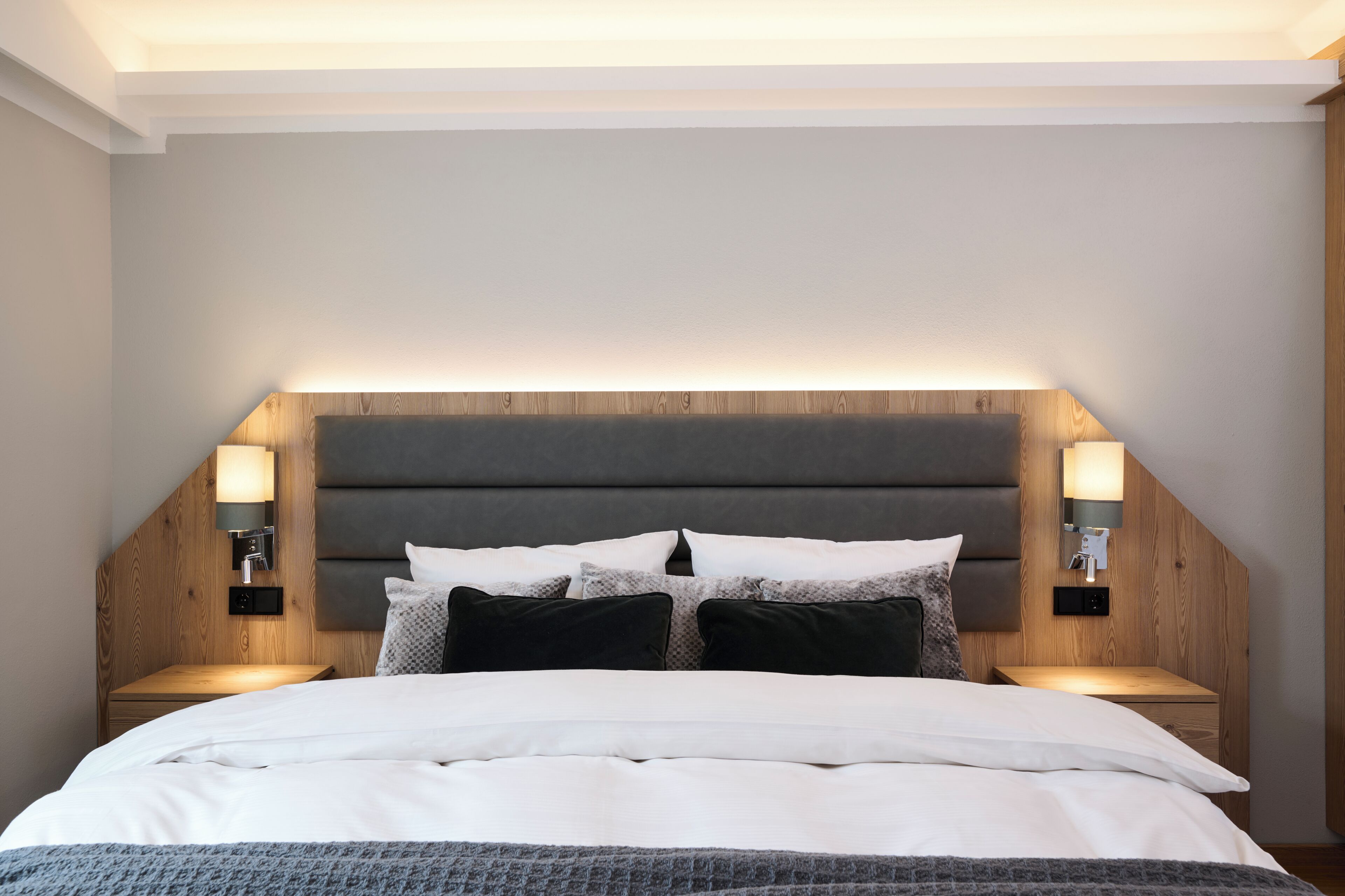 A bedroom with a bed, headboard, bedside tables, and wall-mounted lighting.