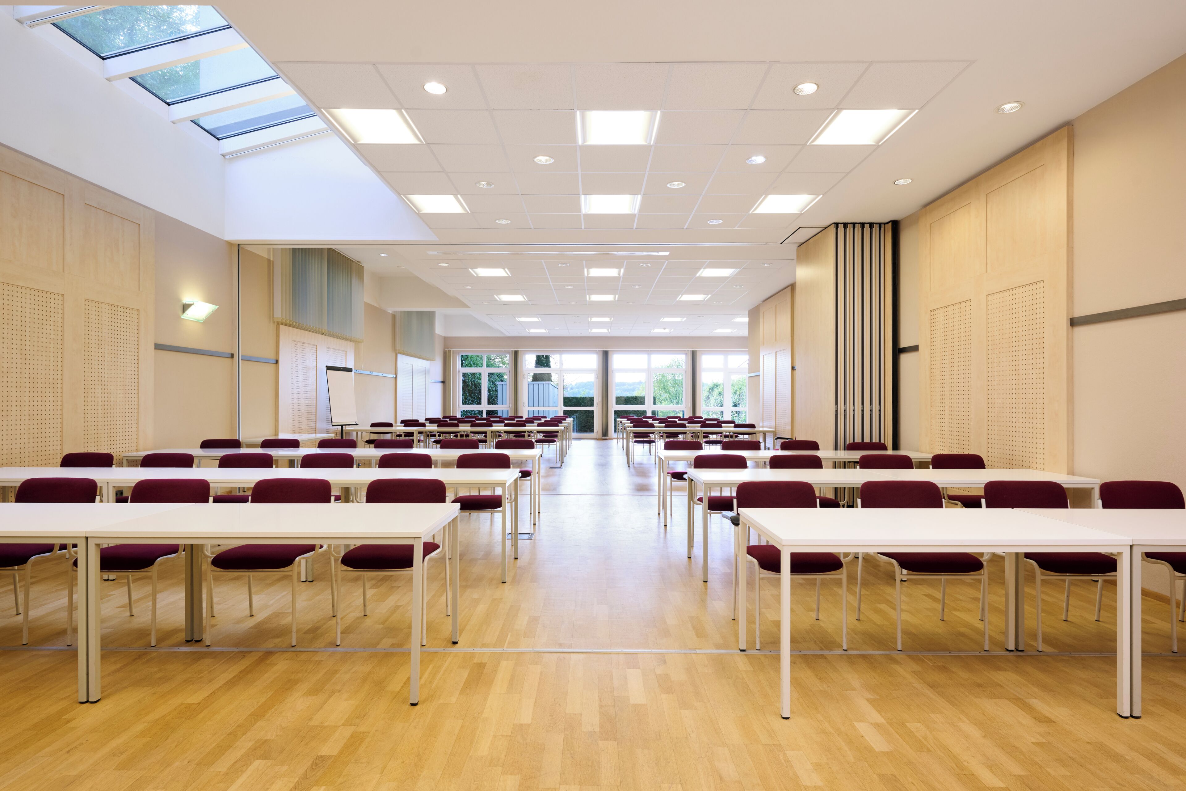 Une salle de conférence équipée de tables et de chaises, dotée d’une verrière et offrant une vue sur l’extérieur.