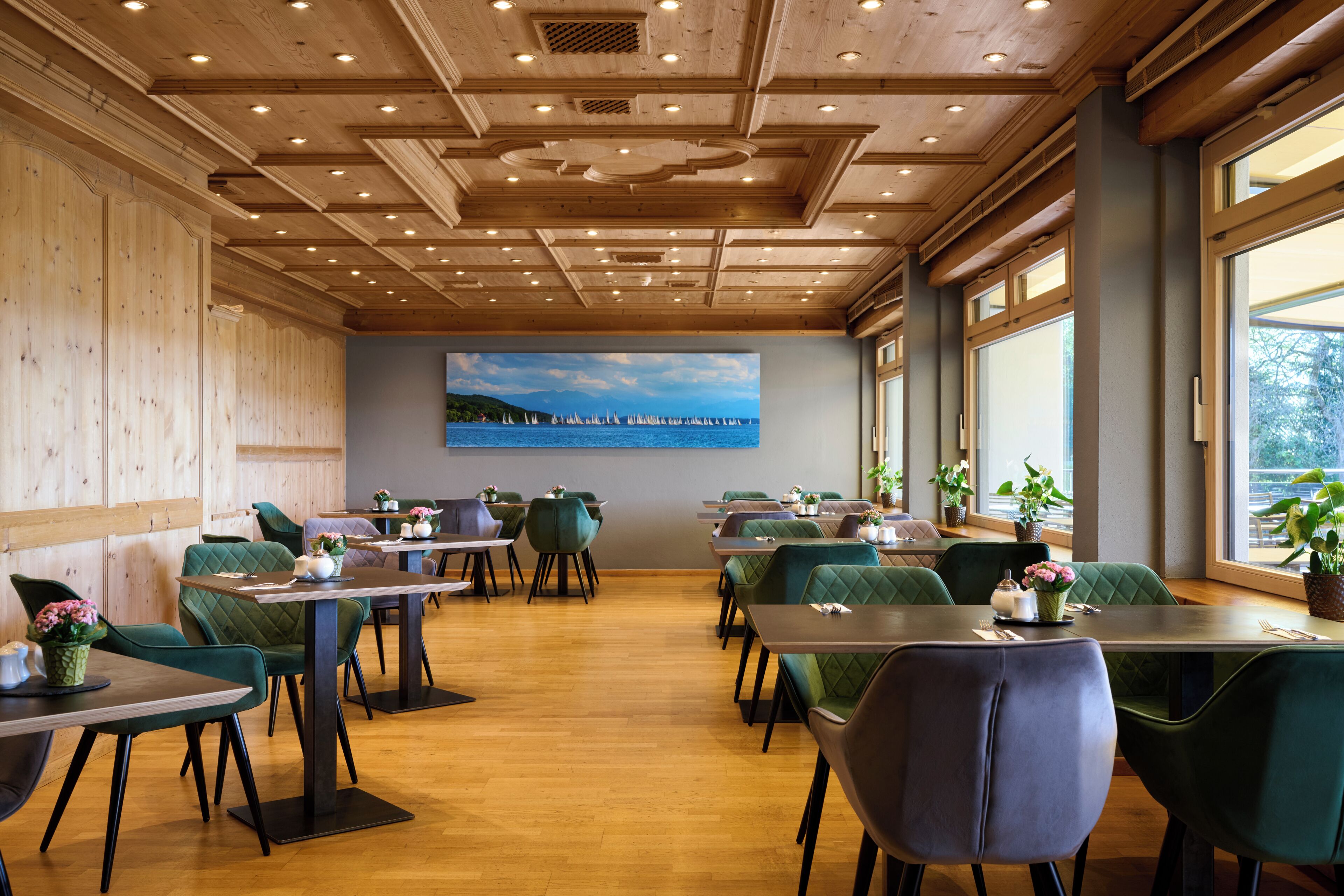 A restaurant with wooden ceiling, green upholstered chairs, and a large window.