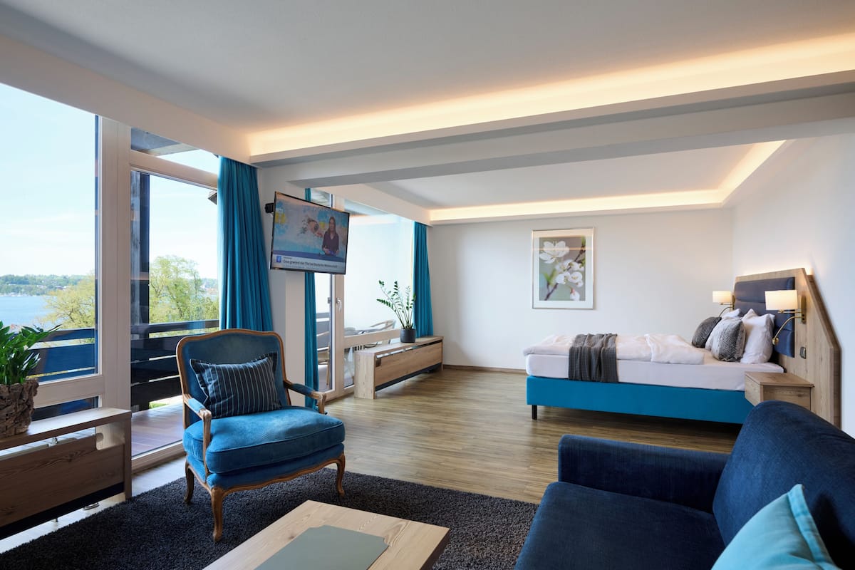 A modern hotel room with a large window, a bed, a sofa, a TV, and a desk.