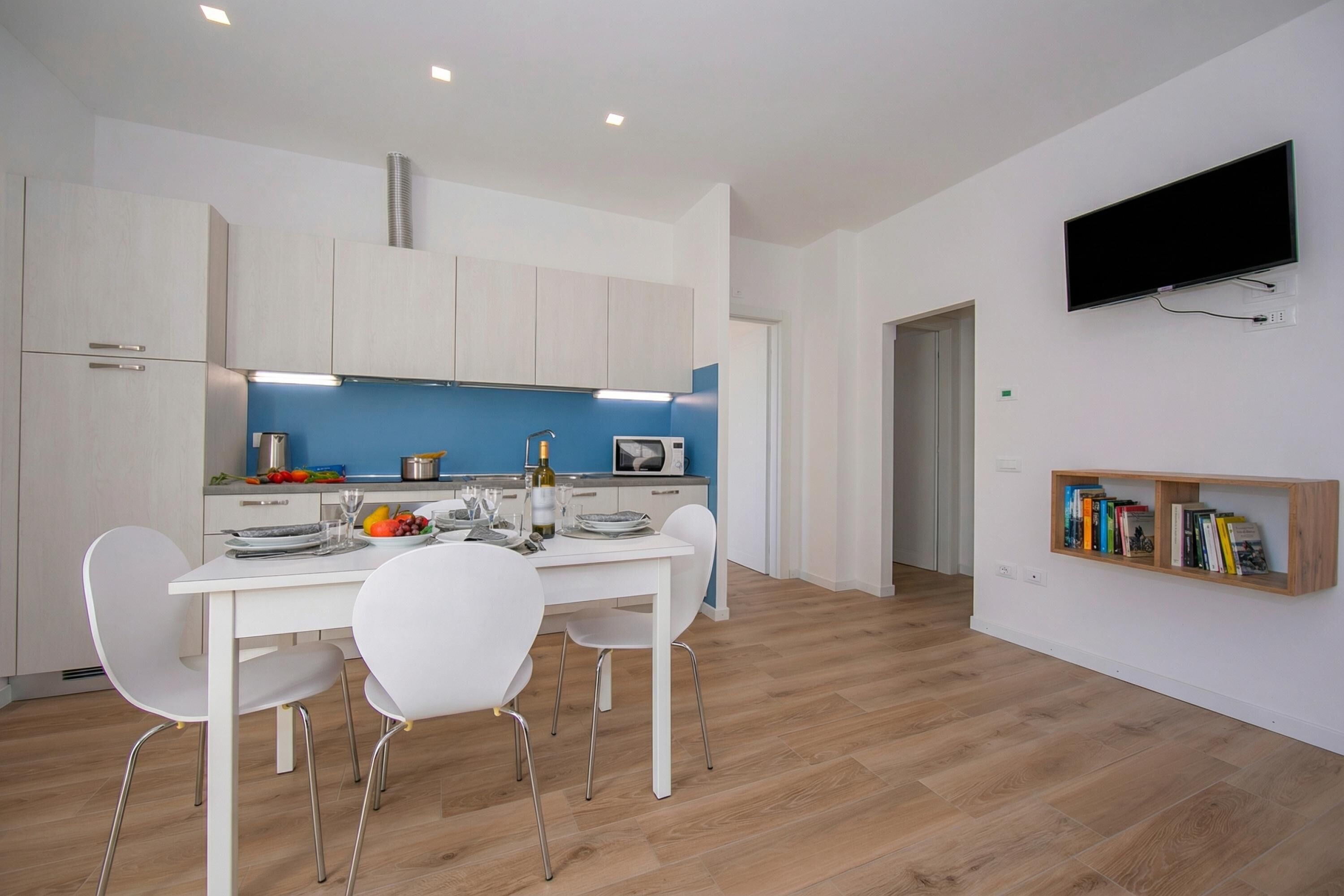 Une cuisine moderne avec des meubles blancs, un pare-feu bleu et un coin repas comprenant une table et des chaises blanches.
