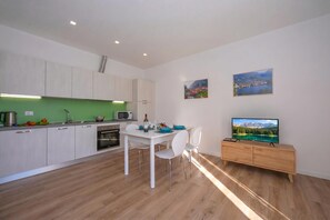 A modern kitchen with white cabinets, a dining area with a white table and chairs, and a TV on a wooden cabinet. - Residenza Giada (Riva del Garda)