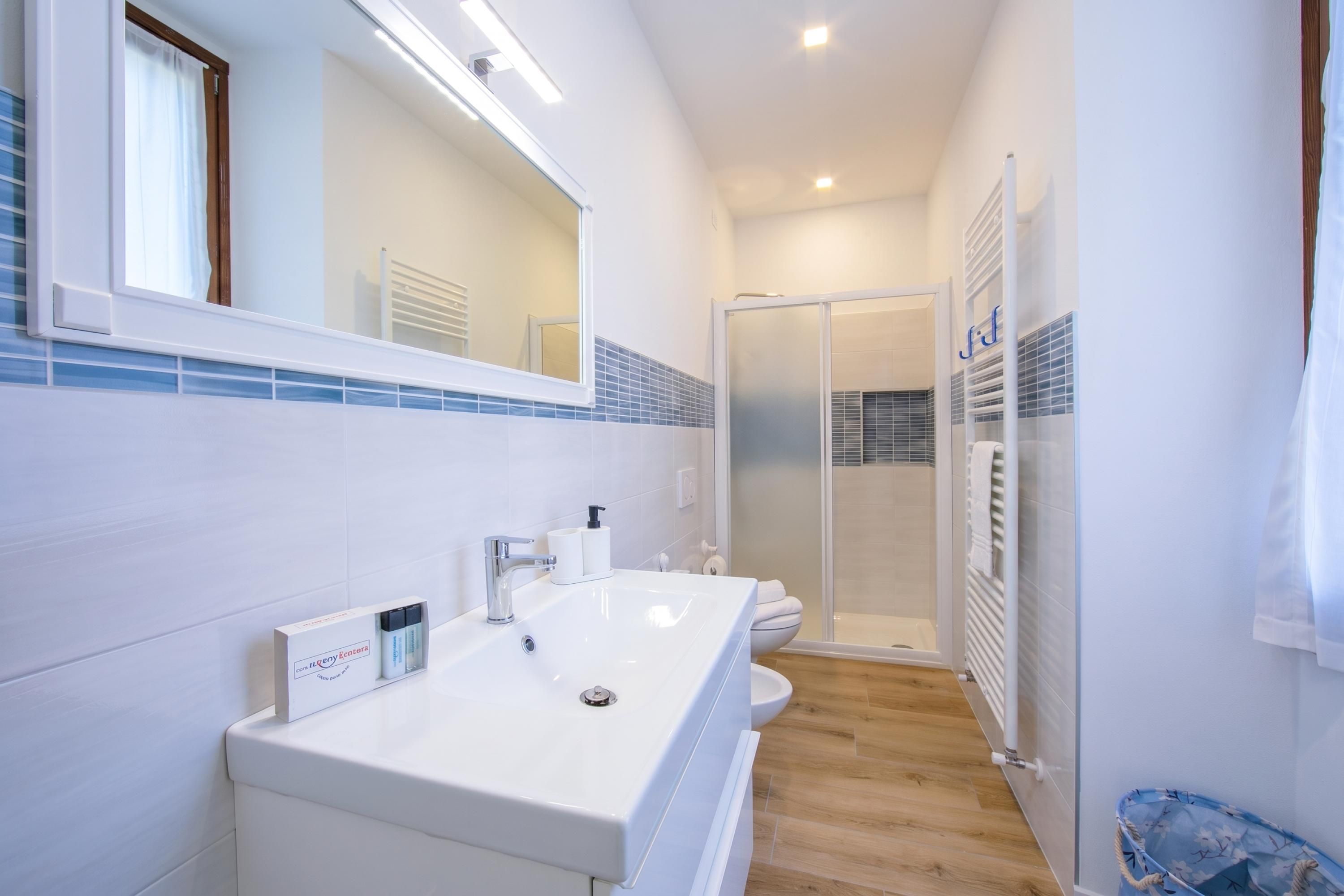 A modern bathroom with a long white sink, a mirror, and a glass shower enclosure.