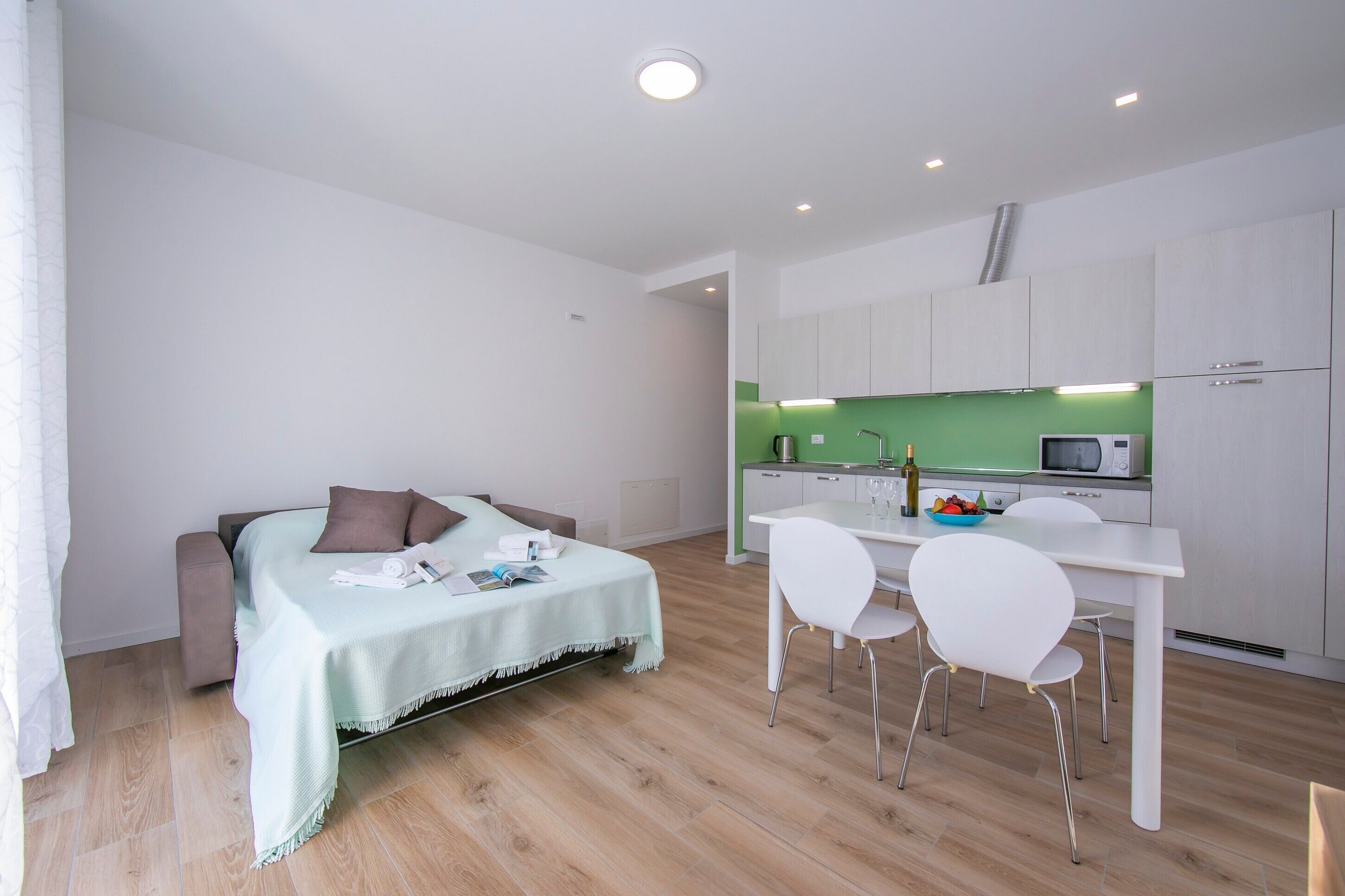 Una habitación moderna con cama, un comedor con sillas, una cocina con microondas y una pared verde.