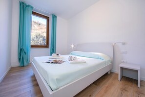 A modern bedroom with a bed, a bedside table, a nightstand, a window with curtains, and a view of the outdoors. - Residenza Giada (Riva del Garda)