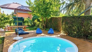 Una piscina con muelle de madera, mesa de picnic techada y sombrilla.