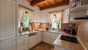 Una cocina con armarios blancos, techo de madera y una ventana con cortinas.