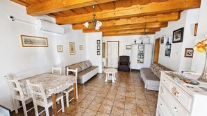 Una habitación con techo de madera, una mesa de comedor con sillas, un sofá, una pequeña mesa redonda y un mueble con cajones.