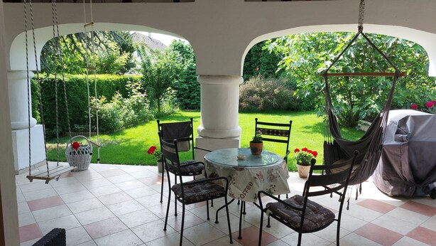 Un patio con una mesa y sillas, una silla colgante, y una vista de un jardín a través de un arco.