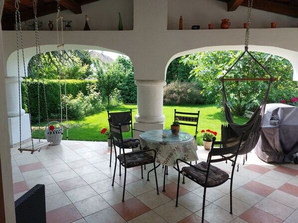 A patio with a table and chairs, a hanging chair, and a view of a garden through an archway.