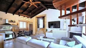 A modern living room with a fireplace, a TV, and a kitchen area with a stove and dining table. - Serenity Villa Retreat in Corfu Close to Resort (Corfu)