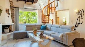 A modern living room with a stone fireplace, a grey sectional sofa, a glass coffee table, and a wooden staircase. - Serenity Villa Retreat in Corfu Close to Resort (Corfu)