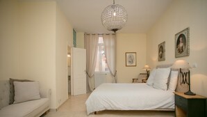 Et soveværelse med seng, natbord, lampe, kommode, et vindue med gardiner og en dør.