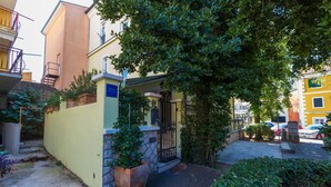 A residential building with a yellow facade, a gated entrance, and a small garden area with potted plants. - Apartments Villa Katarina (Selce)