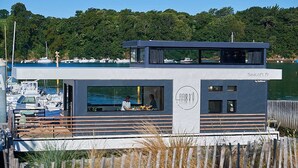 Ein modernes Boot mit überdachter Deckfläche und Panoramafenster, vor Anker in einer Marina mit weiteren Booten.