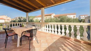 A covered outdoor patio with a table and chairs, a white balustrade, and a view of houses in the background. - Apartment Masholina (Tribunj)