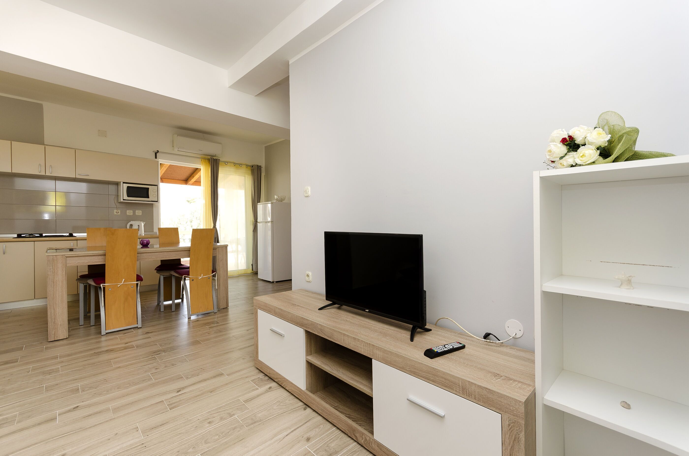 A modern kitchen with a microwave, stove, and dining area. There is a TV on a wooden stand and a remote control on the stand.