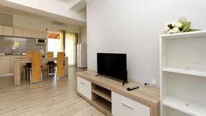 A modern kitchen with a microwave, stove, and dining area. There is a TV on a wooden stand and a remote control on the stand. - Apartment Masholina (Tribunj)