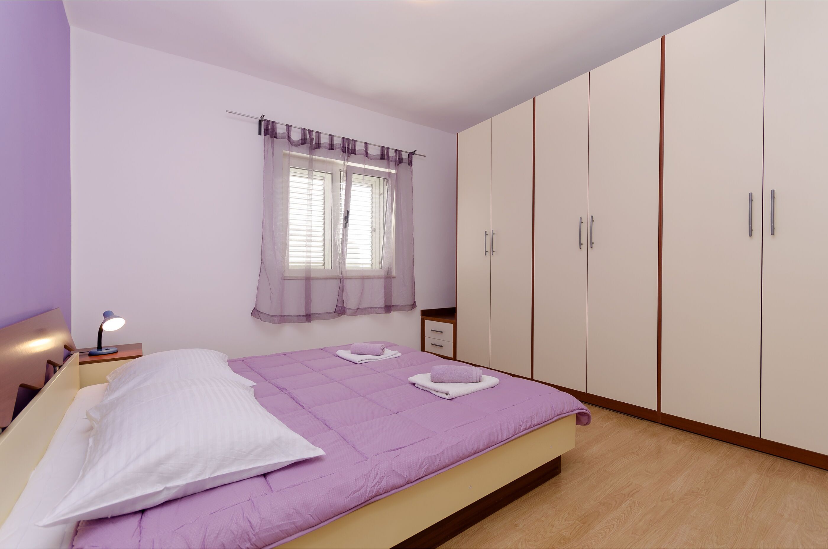 Une chambre à coucher avec un lit, une table de chevet, une fenêtre avec des rideaux et une armoire.