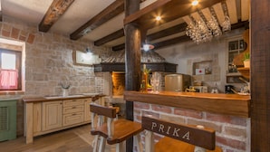 A rustic kitchen with exposed brick walls, wooden beams, and a bar area with stools labeled "PRIKA". - Villa Calandra (Vrana)