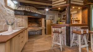 A rustic kitchen with a stone wall, wooden beams, a brick oven, and a bar area with stools. - Villa Calandra (Vrana)