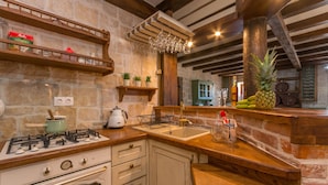 A rustic kitchen with a stone wall, wooden shelves, a gas stove, and a wooden countertop. - Villa Calandra (Vrana)