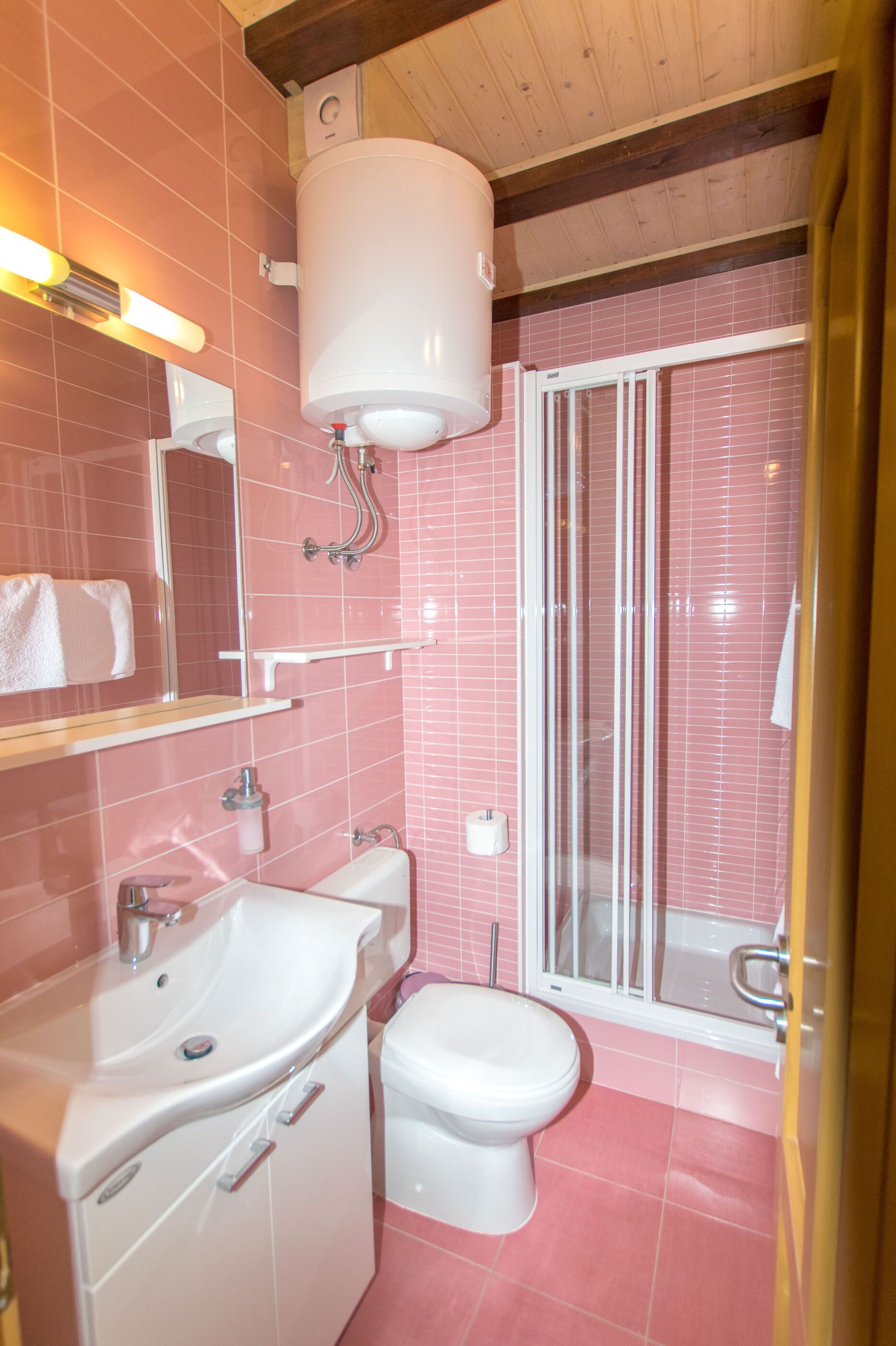 A bathroom with pink tiles, a white sink, a toilet, and a glass shower enclosure.