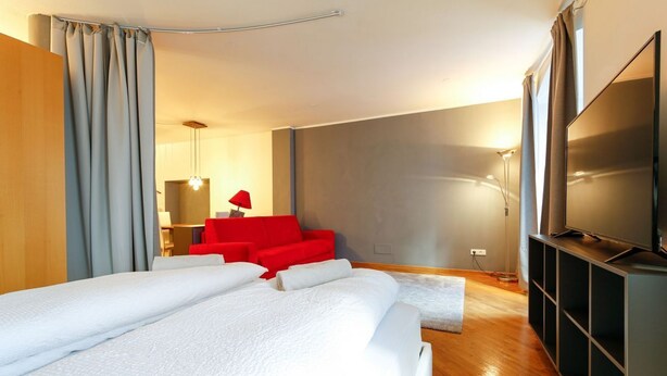 A modern hotel room with a large bed, a red sofa, a TV, and a wooden floor. - "Lauben Uno" New apartment with modern design, in the center of Merano! (Merano)