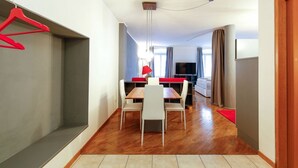 A modern living room with a wooden floor, a dining table with chairs, a TV, and a red hanging chair. - "Lauben Uno" New apartment with modern design, in the center of Merano! (Merano)