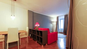 A modern living room with a wooden dining table, white chairs, a red sofa, and a black shelving unit. - "Lauben Uno" New apartment with modern design, in the center of Merano! (Merano)