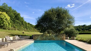 A rectangular swimming pool with clear blue water, surrounded by a stone wall and a grassy area with trees. - Moulin aux Ans, charming gîte in a former schoolhouse (Archignac)