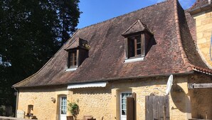 A stone building with a sloped roof, a wooden fence, and a small dock extending into a body of water. - Moulin aux Ans, charming gîte in a former schoolhouse (Archignac)