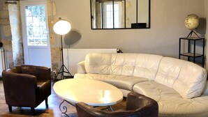 A living room with a white leather sofa, a brown leather armchair, a round coffee table, and a globe on a stand. - Moulin aux Ans, charming gîte in a former schoolhouse (Archignac)