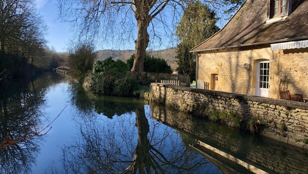 A stone building with a wooden fence and a clear reflection in the water. - Moulin aux Ans, charming gîte in a former schoolhouse (Archignac)