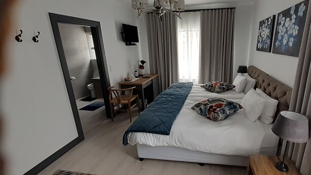Una camera d'albergo con un letto, una scrivania, una sedia, una televisione e una finestra con tende.