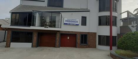 Un edificio moderno con un letrero que dice 'Guesthouse Indongo A Conference'. Tiene un garaje, un ventanal grande y una puerta roja.
