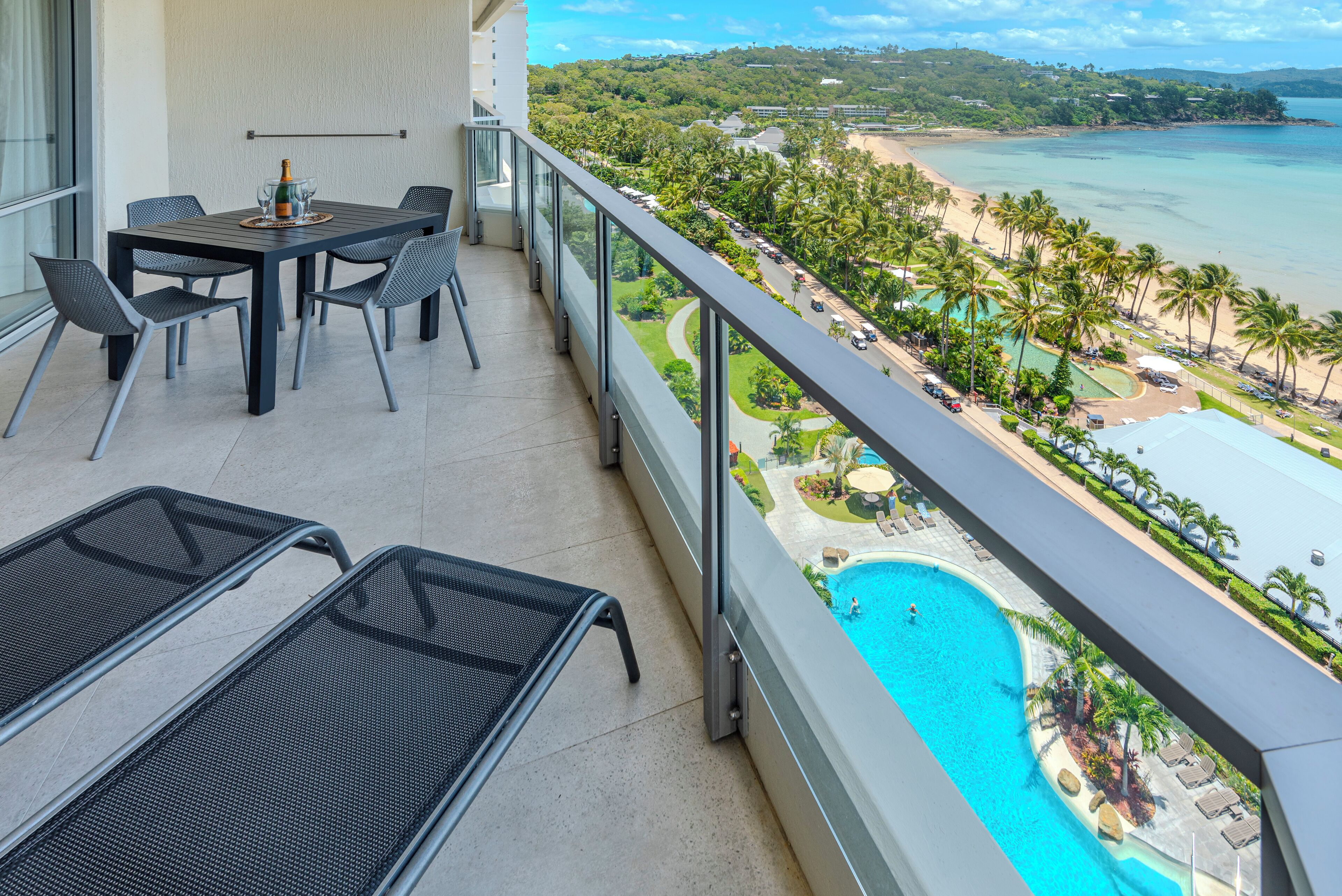 Un balcon avec une table et des chaises, donnant sur une plage et une piscine.